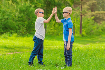 Two blond boys in sunglasses give five their hands in the summer park. Toned