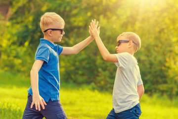 Two blond boys in sunglasses give five their hands in the sunny park