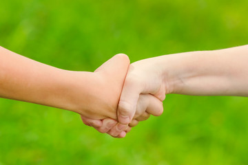 Gesture of handshake of boys on a blurred green background. Toned