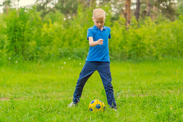 Blond boy in a blue T-shirt playing football in the park