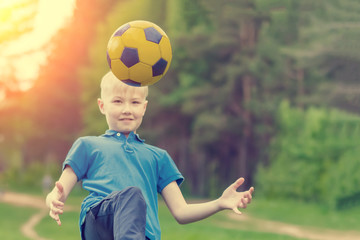Blond boy in a blue T-shirt kicks the ball with his knee in the park