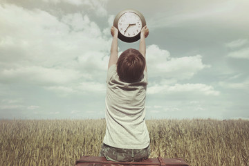 Little boy raises in the sky a watch in a surreal landscape