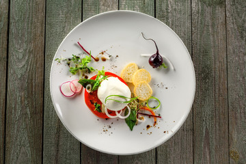 Classic Italian cuisine meal made of mozzarella, tomato and herbs on a table. Caprese salad on a white round plate.