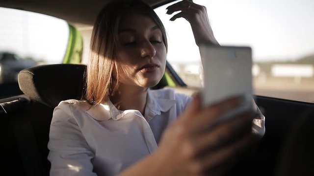 Beautiful business woman traveling in a taxi to an important meeting and corresponding with colleagues using a smartphone