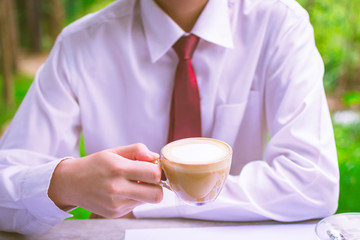Enjoying fresh coffee. Confident young charming man in formal wear holding coffee cup and sitting on garden