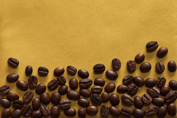 Roasted coffee beans on textured gold background, close-up, view from above