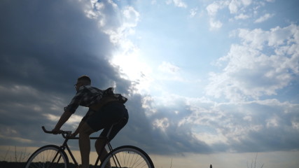 Fototapeta na wymiar Silhouette of young man riding at vintage bicycle with beautiful sunset sky at background . Sporty guy cycling in the country road. Male cyclist riding bike. Healthy active lifestyle Slow motion
