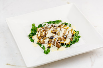 Italian ravioli with fresh roasted mushrooms and creamy parmesan cheese sauce decorated with spinach on white plate.