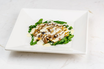Italian ravioli with fresh roasted mushrooms and creamy parmesan cheese sauce decorated with spinach on white plate.