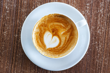White coffee cup on a saucer with a heart shape in the latte foam