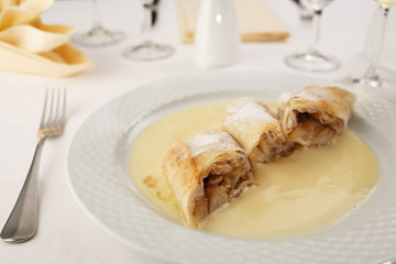 Apple pie slice with vanilla mousse arranged on a plate, Wineglass in background, Traditional dessert in elegant setting, Selective focus with soft light