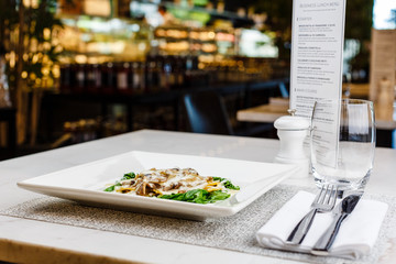 Italian ravioli with fresh roasted mushrooms and creamy parmesan cheese sauce decorated with spinach on white plate.