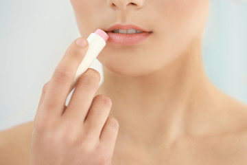 Closeup view of beautiful young woman applying lipstick, light background