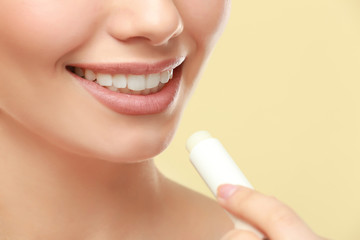 Closeup view of beautiful young woman applying lipstick, color background