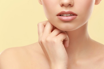 Fototapeta na wymiar Closeup view of beautiful young woman with natural lips makeup touching neck on color background