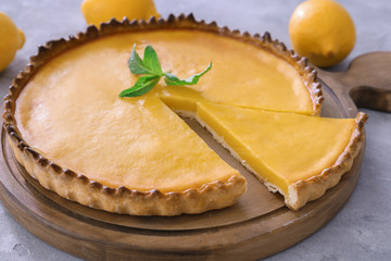 Wooden board with delicious lemon pie on gray table, closeup