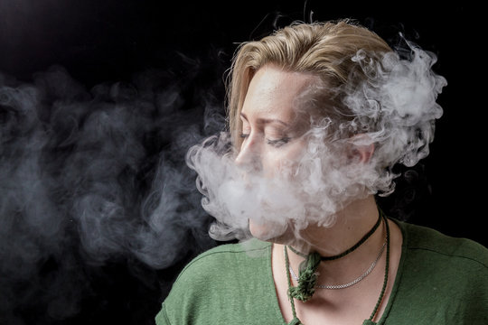 Young woman exhaling nicotine smoke from electronic cigarette