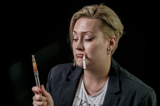 Female is questioning about vaping electronic cigarette while holding tobacco cigarette between her teeth