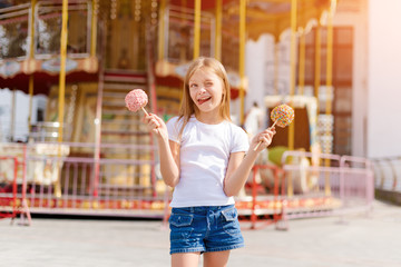 Cute little girl eating candy apple and posing at fair in amusement park.