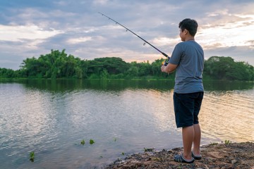 Young man fishing on a river at beautiful evening sky.