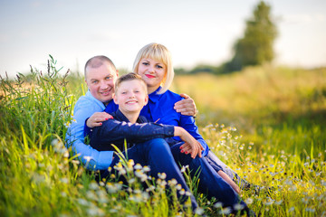 Naklejka na ściany i meble Happy family in the evening in the field among wild flowers, embrace and smile