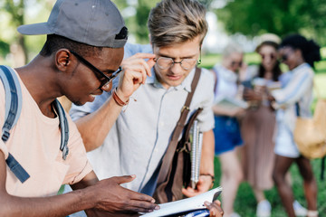 two multiethnic boys reading book together in park