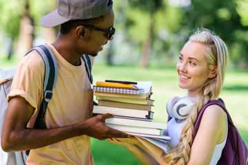 side view of happy young multiethnic couple holding books together while standing in park