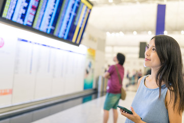 Woman checking flight schedule with cellphone and display board