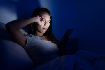 Woman suffer from headache with using mobile phone on bed at night