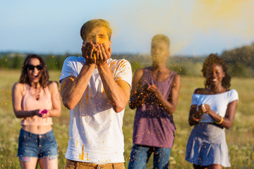 young multiethnic friends blowing powder from palms at holi festival