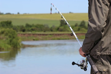 Рыболов со спиннингом в руке ловит рыбу на берегу озера