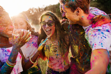 cheerful young multiethnic friends with colorful paint on clothes and bodies having fun together at...