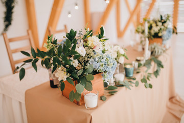 Fototapeta na wymiar In the wedding banquet area there are wooden tables with tablecloths, on tables there are compositions of flowers and greens, candles, cutlery, on plates lie napkins with name cards
