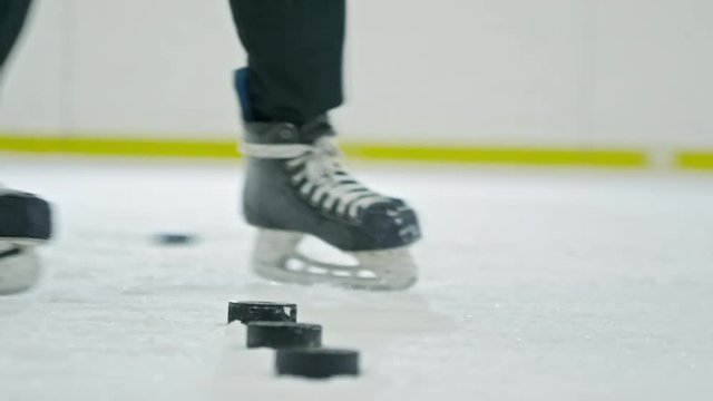Low-section of unrecognizable hockey player skating on ice and shooting six pucks in row during practice