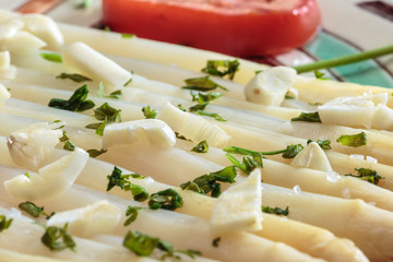 Detail of vegetarian recipe made of white asparagus and tomato slices seasoned with garlic and parsley, plated in a decorated ceramic dish. Tasteful and healthy food