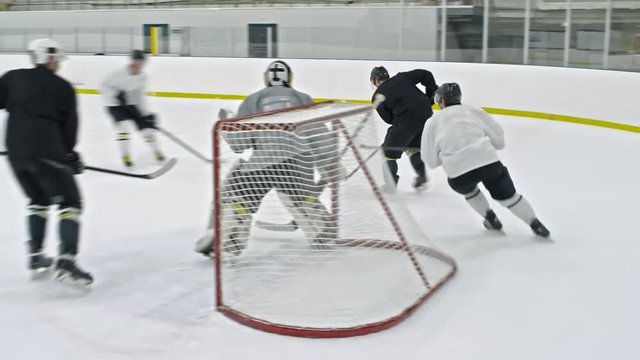 PAN of male hockey forward in black uniform dribbling puck behind net, then scoring tricky goal with help of his teammate