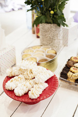 Candy bar Table with sweets, candies, dessert. French meringue cookies in red high plateau, tray. Egg white sweets, biscuits and flowers on a white wooden table