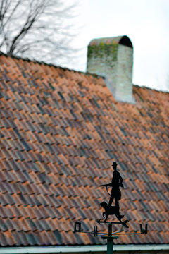 Windvane with hunter and dog opposite the traditional tile roof somewhere in Netherlands