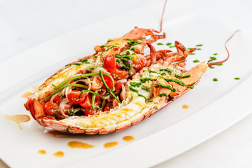 Italian cuisine. Whole lobster baked and sliced in half Served with tomato salad and sauce on white...