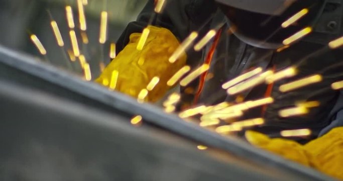 Tilt up of young pretty female worker welding metal material with torch and then taking off protective mask