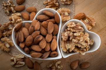 Rustic image of two heart shaped bowls of almonds and walnuts. The walnut bowl is smaller and fits in the shape of the bigger almond bowl. Source of manganese, Vitamin E, Omega 3 fatty acids, etc