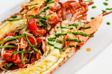 Italian cuisine. Whole lobster baked and sliced in half Served with tomato salad and sauce on white plate