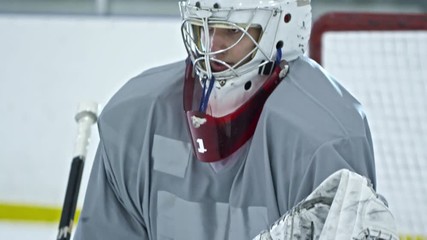 Tilt up of concentrated hockey goalie in protective gear standing before net and failing to catch puck with glove during practice - Powered by Adobe