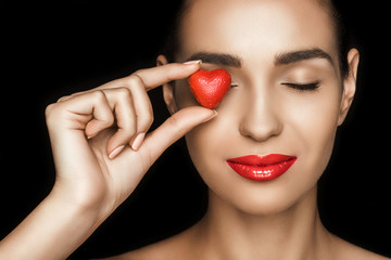 attractive woman with closed eyes holding red heart shaped candy, isolated on black