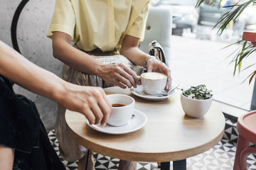 Hands of two cropped unrecognisable women holding cups of coffee at cafe.