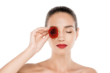 attractive naked woman with closed eyes holding red rose in front of eye, isolated on white
