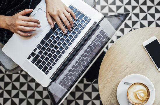 From above photo of hands of cropped unrecognisable woman typing on laptop and sitting at coffee shop.
