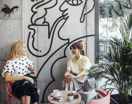 Two pretty Caucasian women girlfriends sitting at coffee shop and chatting.