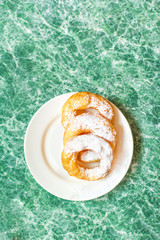 Fresh donuts topped with white sugar powder on a plate on colorful background close up, top view.