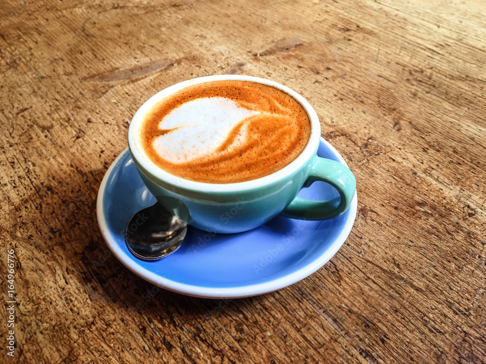 Poster Coffee cup with heart pattern  in coffee shop on wooden table with vintage style effect, close up with copy space .